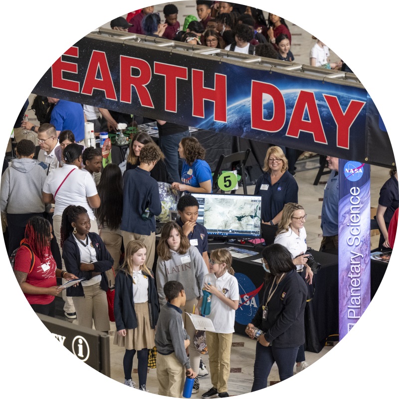 image of a gathering of people in front of and understand a large banner that reads Earth Day